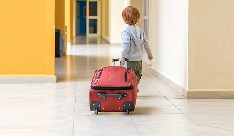 Little boy pulling red suit case down hallway.