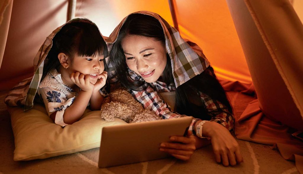 Mother and daughter watching a movie together on the floor with a tablet under an indoor tent