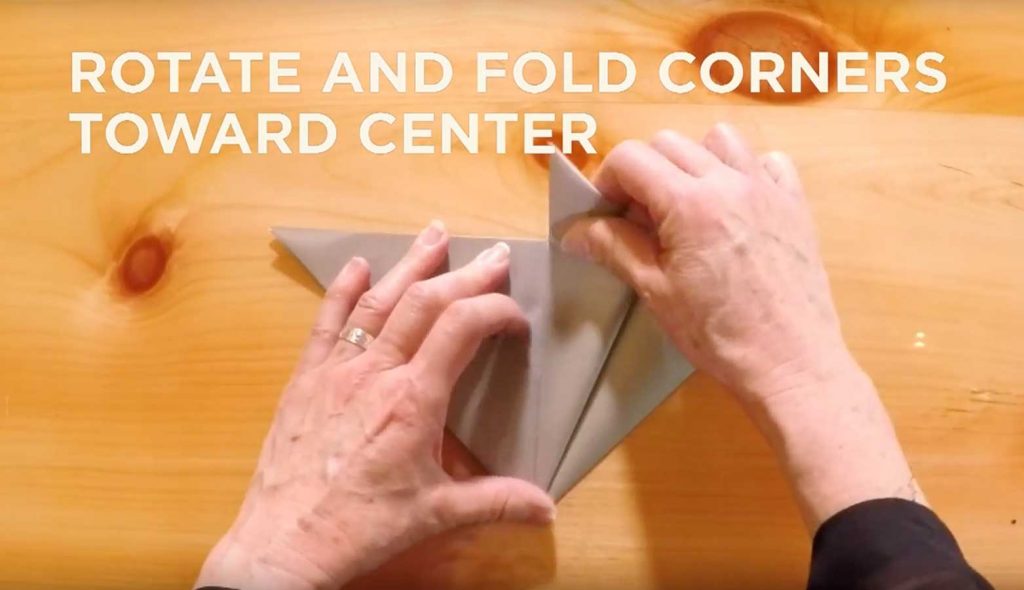 Paper being folded with text saying, "Rotate and fold corners toward center."