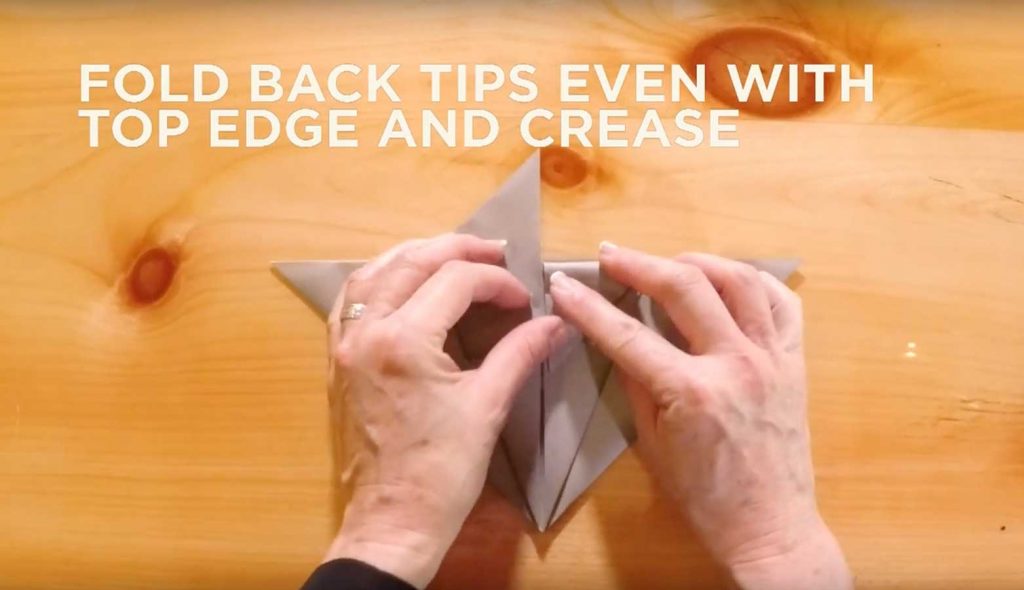 Paper being folded with text saying, "Fold back tips even with top edge and crease."