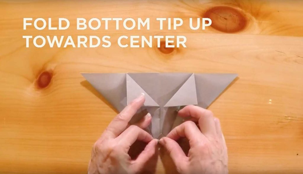 Paper being folded with text saying, "Fold bottom tip up towards center."