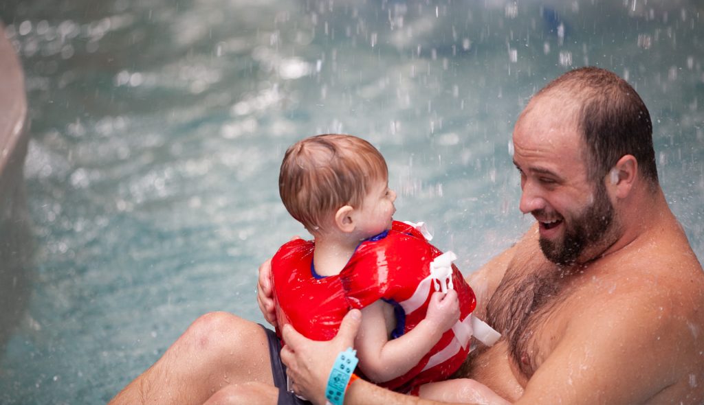 Father and his toddler playing in a shallow pool at a water park.