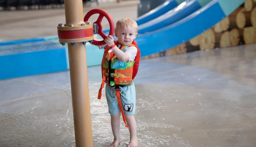Toddler wearing a safety water vest while playing with a wheel at a water park