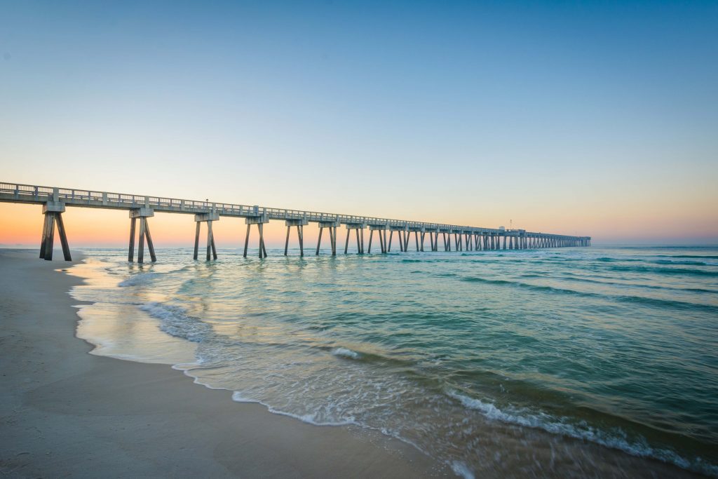 Sunrise at Panama City Beach with pier in the background as water splashes the sand.