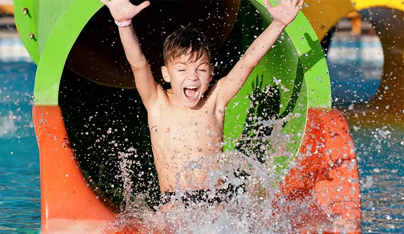 Boy with hands up coming out of a water slide